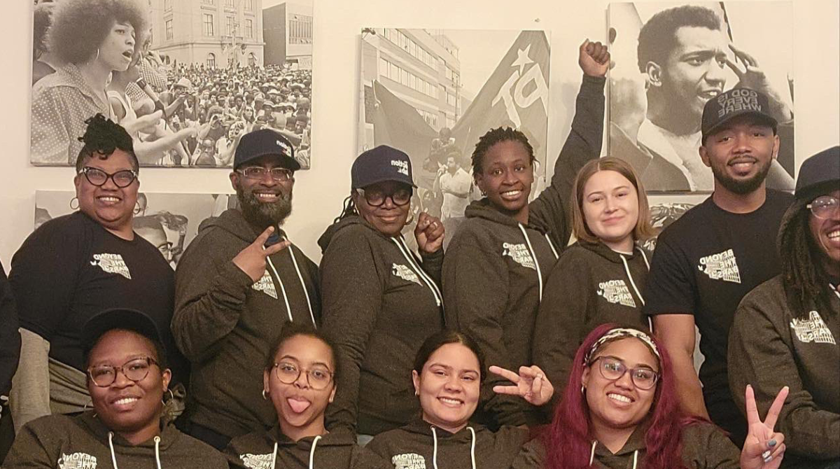 Group of people in Beyond the Bars hoodies in front of pictures of Black revolutionary leaders